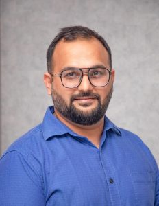 corporate headshot of a man with glasses and a beard