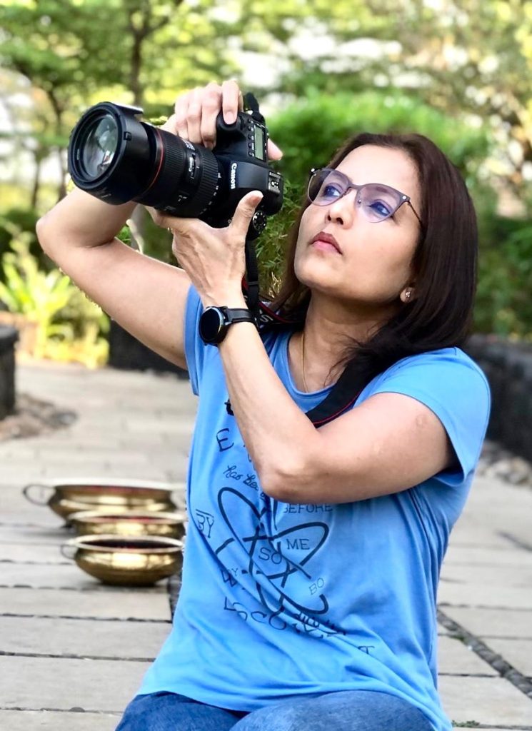 Photo of Tanuja Uchil outdoors in a blue tshirt looking into a camera