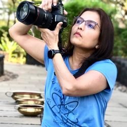 Photo of Tanuja Uchil outdoors in a blue tshirt looking into a camera