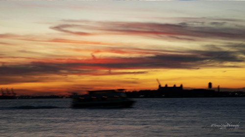 scenery of a boat in the water at sunset with a city in the background