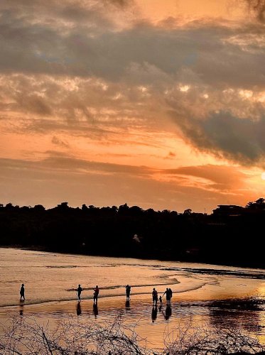 scenery of people walking on the beach at sunset with a cloudy sky