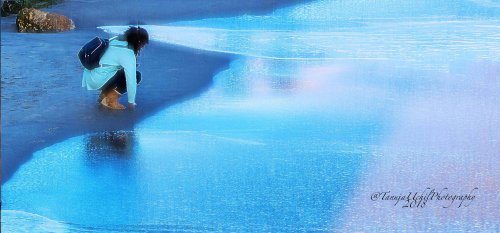 scenery of a woman kneeling on the beach with her surfboard