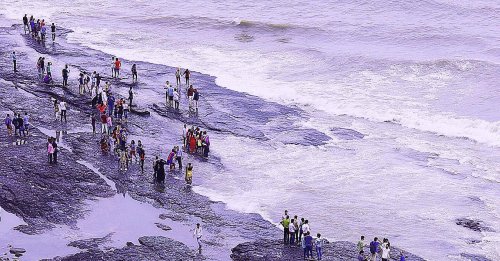 scenery of people standing on a rocky beach near the ocean