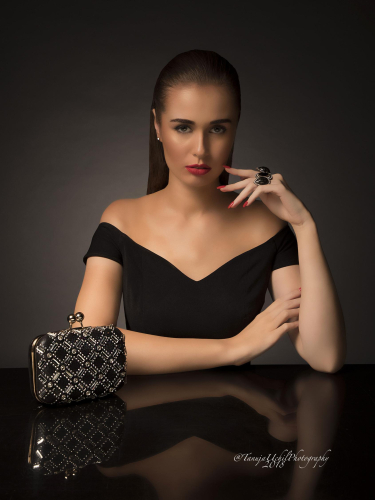 corporate headshot of a woman in a black dress with a clutch