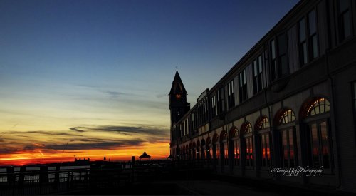 scenery of a clock tower at sunset with a person walking on a boardwalk